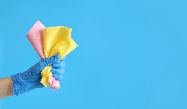 Toallitas limpiadoras de viscosa. La mano de una mujer en un guante de látex azul sostiene varias toallitas limpiadoras. Mano con un trapo para limpiar sobre fondo azul. El concepto de limpieza profesional. espacio de copia - Foto, imagen