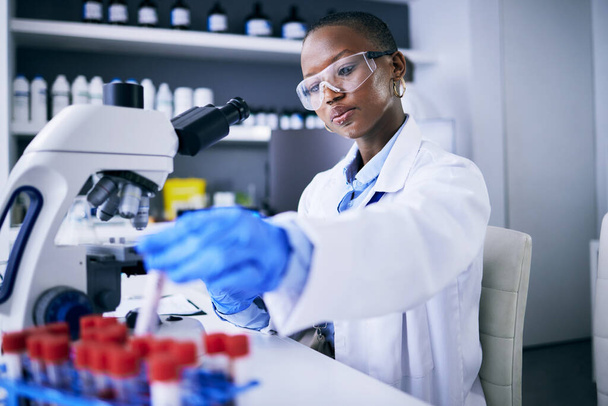 Blood test, microscope and science woman in laboratory for cancer research, medical analysis and dna test. Biotechnology, red liquid and scientist, doctor or african person, check tube in healthcare. - Foto, Imagem