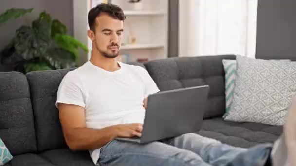Νεαρός Ισπανός που χρησιμοποιεί φορητό υπολογιστή καθισμένος στον καναπέ στο σπίτι - Πλάνα, βίντεο