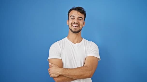 Joven hombre hispano sonriendo confiado haciendo gesto telefónico con la mano sobre fondo azul aislado - Imágenes, Vídeo