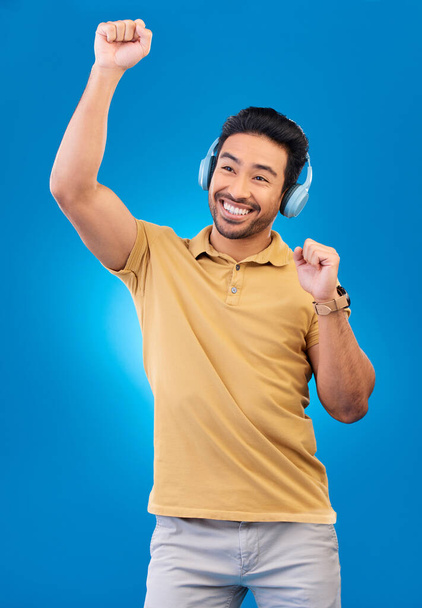 Happy, zene és tánc fülhallgatóval vagy ázsiai férfi kék háttérben a szórakozás. Energia, srác és dal fülhallgató boldogsággal streaming online rádió tech stúdióban - Fotó, kép