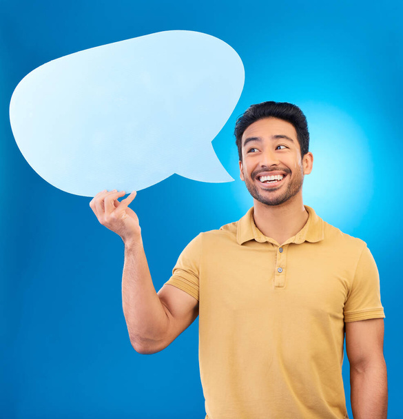 Man, speech bubble and thinking in studio with smile for opinion, social media and poster by blue background. Indian guy, student and model with paper, mock up space and cardboard sign for promotion. - Foto, imagen