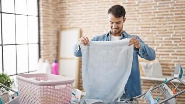 Mladý hispánec muž usměvavý sebevědomě visí oblečení na prádelní šňůře v prádelně - Záběry, video