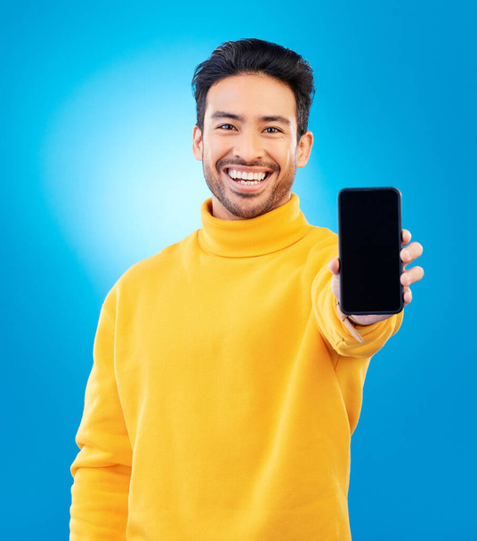 Marketing, portrait of man with smartphone and blue background happy for online communication. Tech app or social networking, advertising or branding and male person with cellphone screen in studio. - Foto, Bild