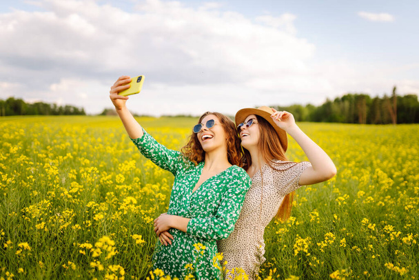 Selfie time.Two  Young woman takes a selfie while walking flowering field. Nature, vacation, relax and lifestyle. Summer landscape. - Photo, Image