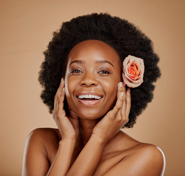 Happy, flower and portrait of a black woman with skincare, clean glow and wellness. Smile, touching face and an African model with floral beauty for skin isolated on a brown background in a studio. - Zdjęcie, obraz