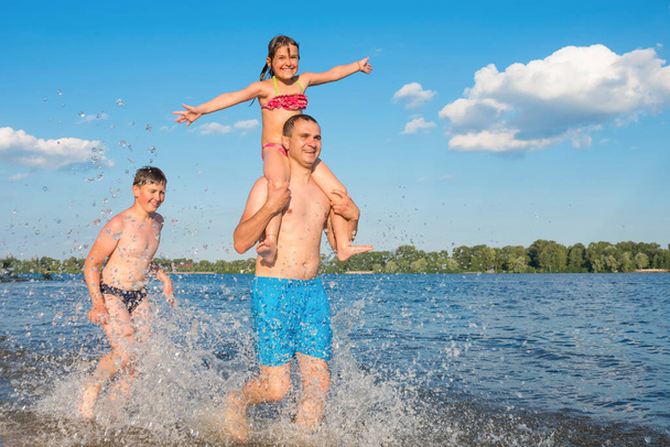 Happy family running on the water on the beach on a sunny day. Games in the water, travel, rest, vacations. Family travel concept - Fotografie, Obrázek