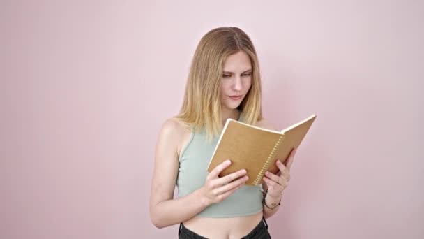 jong blond vrouw lezen boek doen duim omhoog gebaar glimlachen over geïsoleerde roze achtergrond - Video