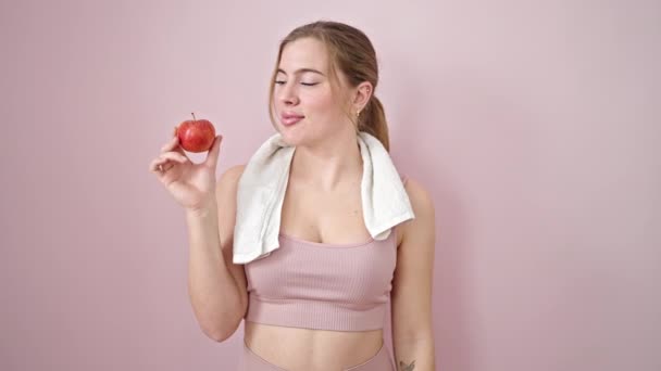 jong blond vrouw doen sterk gebaar met arm houden appel over geïsoleerde roze achtergrond - Video