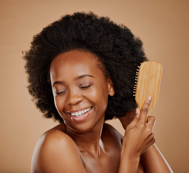 Happy black woman, afro and brush hair in studio, brown background and treatment of curly texture. Natural beauty, smile and face of young african female model with comb, hairstyle or aesthetic tools. - Foto, Imagem