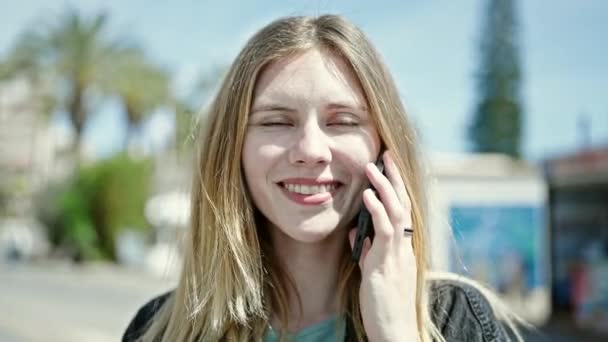 Молодая блондинка улыбается уверенно разговаривая по смартфону на улице - Кадры, видео