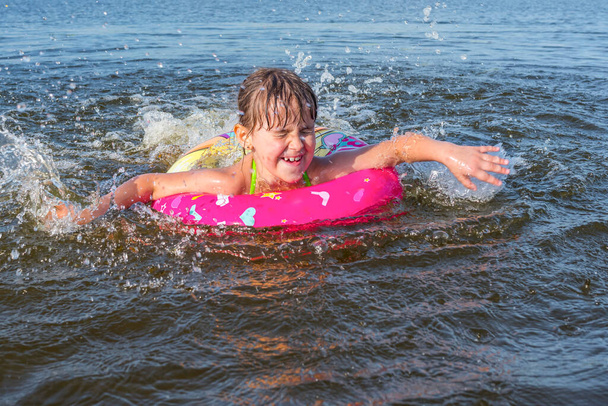 Happy little girl playing on a pink rubber ring on the river. - Φωτογραφία, εικόνα