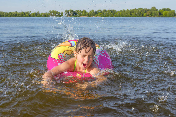 Little girl on the water with a rubber ring. The child learns to swim. - Foto, afbeelding