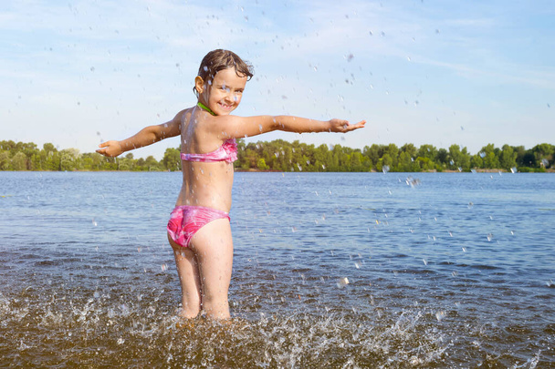 Happy child plays with splashes of water on the river bank. - Foto, Imagem