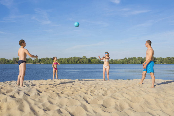 Gelukkige familie spelen beachvolleybal bij de rivier op een zonnige dag. levensstijl. - Foto, afbeelding