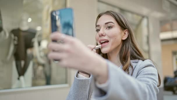 Genç İspanyol kadın akıllı telefonu ayna olarak kullanıyor. Sokakta makyaj dudakları. - Video, Çekim