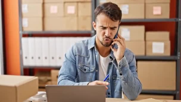Joven hombre hispano comercio electrónico trabajador de negocios usando portátil hablando en smartphone discutiendo en la oficina - Metraje, vídeo