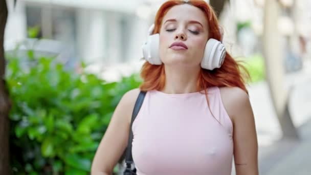 Genç kızıl saçlı kadın sokakta rahat bir ifadeyle müzik dinliyor. - Video, Çekim