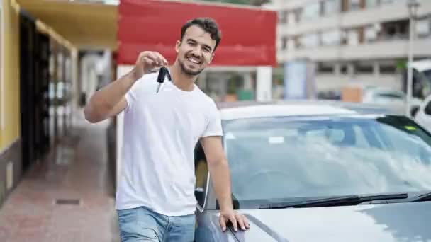 Молодий іспаномовний чоловік посміхається впевнено тримає ключ від нової машини на вулиці
 - Кадри, відео