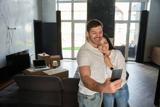 Junges Paar macht ein Selfie im Wohnzimmer seiner Wohnung - Foto, Bild