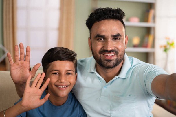 Gelukkig glimlachende Indiase vader met zoon praten videogesprek door het houden van camera thuis - concept van lange afstand relatie, sociale media live en cyberspace. - Foto, afbeelding