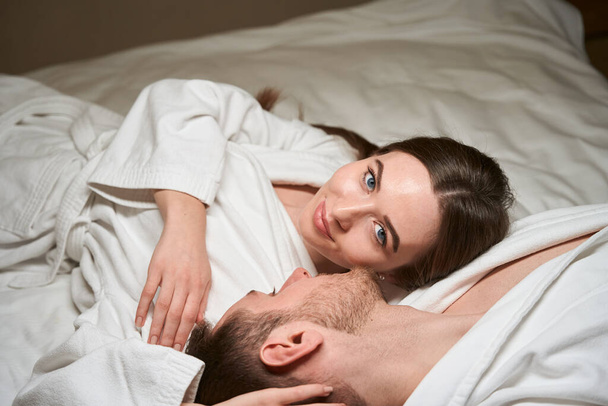 Ηρεμία χαλαρή νεαρή γυναίκα που βρίσκεται κοντά στο σύντροφό της στο άνετο κρεβάτι - Φωτογραφία, εικόνα