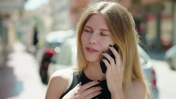 Fiatal szőke nő mosolygós magabiztos beszél az okostelefon az utcán - Felvétel, videó