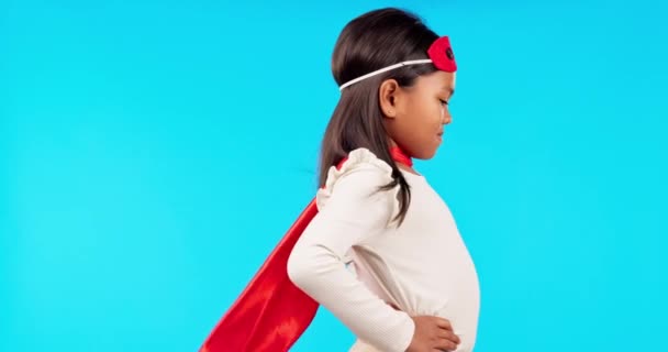 Superhero, fantasy and girl child in a studio with a cape and face mask with wind blowing. Save, happy and profile of a kid model in cosplay outfit or costume isolated by blue background with mockup - Footage, Video