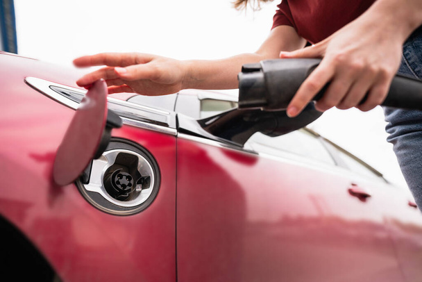Woman with smartphone charging red electric car - Foto, imagen