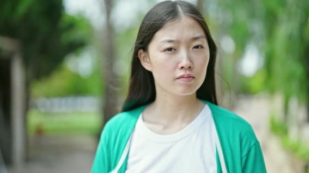 Fiatal kínai nő áll komoly kifejezés a parkban - Felvétel, videó