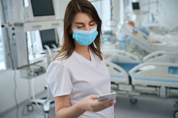 Сосредоточенная женщина-врач пишет с пациенткой на смартфоне и дает онлайн-консультацию в клинике - Фото, изображение
