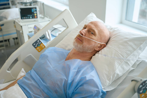 Male patient getting supplemental oxygen through nose tubes while lying on the bed in intensive care at hospital - Fotó, kép