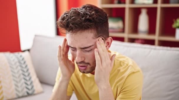 Joven hispano sufriendo de dolor de cabeza sentado en el sofá en casa - Imágenes, Vídeo