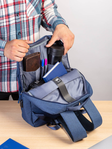ラップトップ、財布、ノートパッドも含まれているバックパックからコーヒーマグカップを取り出す若い男性学生のクローズアップ - 写真・画像