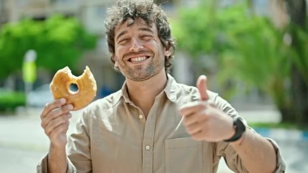 Een jonge Spaanse man die donut vasthoudt en een gebaar maakt op straat. - Video