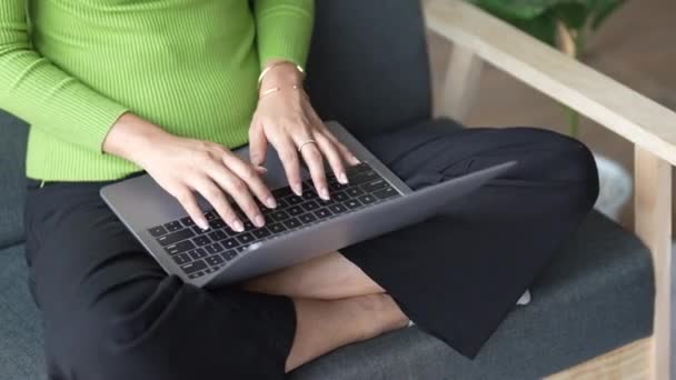 De cerca la mano de la joven hembra usando el ordenador portátil mientras está sentado en el sofá, escribiendo en el ordenador portátil. - Metraje, vídeo