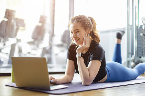 υγιής γυναίκα απολαμβάνουν το διάστημα χαλαρώστε φρένο στο γυμναστήριο γυμναστήριο αθλητικό σύλλογο χρησιμοποιώντας φορητό υπολογιστή βλέποντας online περιεχόμενο. - Φωτογραφία, εικόνα