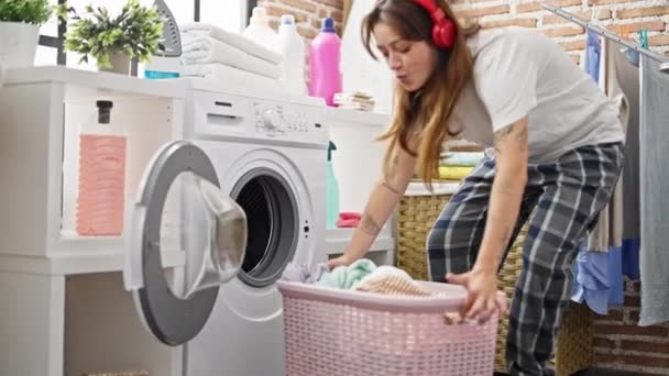 Młoda piękna Latynoska słuchająca muzyki myjącej ubrania w pralni - Materiał filmowy, wideo