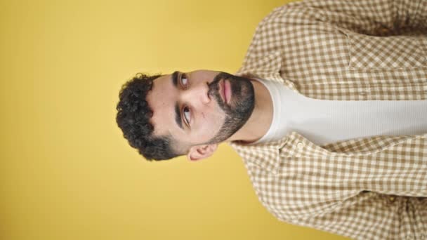 Νεαρός Ισπανόφωνος άντρας χαμογελάει με αυτοπεποίθηση κοιτάζοντας πάνω από απομονωμένο κίτρινο φόντο - Πλάνα, βίντεο