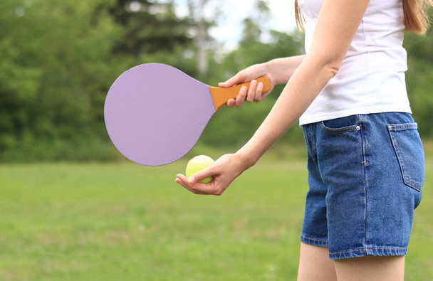 Doğanın arka planında tahta raketle paddleball oynamak. Tenis oynamak için tahta kürek ve bir kızın elinde top. Açık hava oyunları. Yakın plan. - Fotoğraf, Görsel