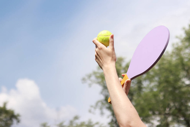Parkta tahta bir raketle tenis oynamak. Plaj raketi ve yakın plan tenis topuyla kadın eli. Açık hava oyunları - Fotoğraf, Görsel