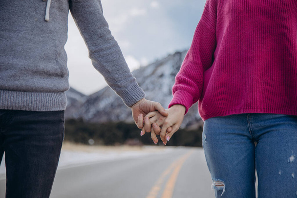 Nuori mies ja nainen kädestä pitäen talvimetsässä. Pari rakastavaista kävelee tiellä. - Valokuva, kuva