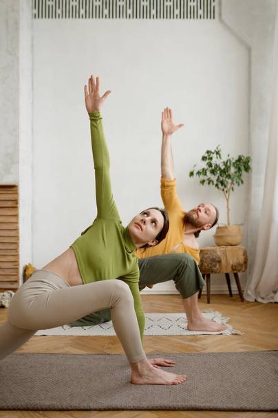 Jonge aantrekkelijke familie paar oefenen yoga stretching staande in Utthita Parshvakonasana pose. Workout thuis, gezonde levensstijl en lichaamsverzorging concept - Foto, afbeelding