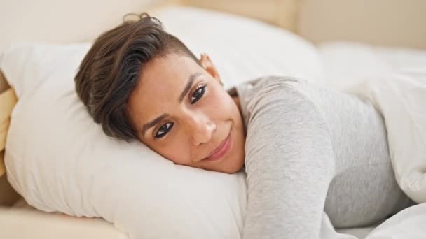 Nuori kaunis latino nainen hymyilee luottavainen makaa sängyllä halaus tyyny makuuhuoneessa - Materiaali, video