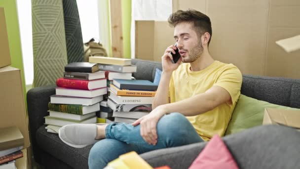 Joven hombre hispano hablando en un smartphone sentado en un sofá celebrando en un nuevo hogar - Metraje, vídeo