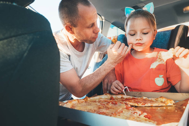 Father wiping gently daughter's mouth while eating just cooked Italian pizza during family car trip brake stop. Happy family moments, childhood, fast food eating or auto journey lunch break con - Foto, Imagen