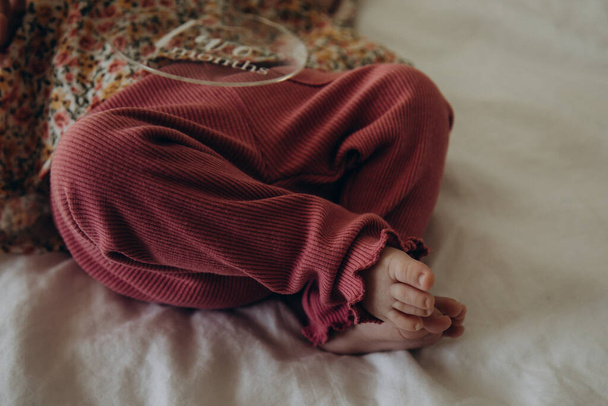 mujer embarazada sosteniendo zapatos de bebé piernas de una chica en una cama recién nacida - Foto, imagen