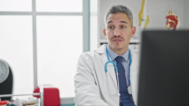 Nuori latino mies lääkäri käyttää tietokonetta ottaa lääkärin konsultointi klinikalla - Materiaali, video