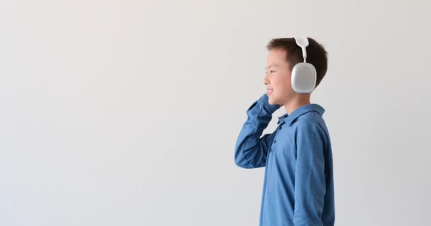 Aziatische jongen verloren in de beklijvende melodieën op een ongerepte witte achtergrond. Met een gestroomlijnde koptelefoon die zijn oren omarmt, wordt hij één met de muziek. - Video