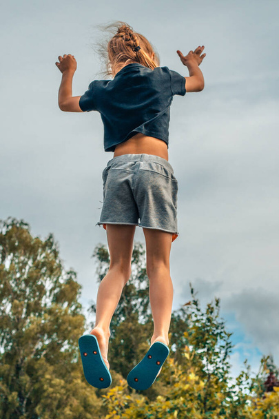 A child jumps on a trampoline. The girl jumped in the air. A child with positive emotions jumps. Jumping on a trampoline can be a wonderful and enjoyable activity for children, promoting physical - Foto, Imagen